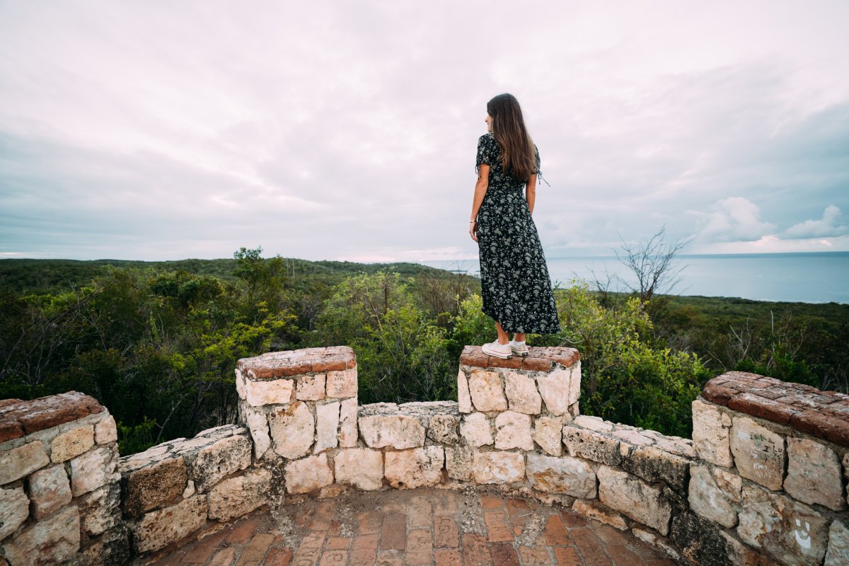 A woman peers over Guánica Dry Forest from the top of Fuerte Capron.