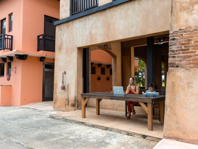 A woman and young boy sit at a desk overlooking a historic street in Puerto Rico.