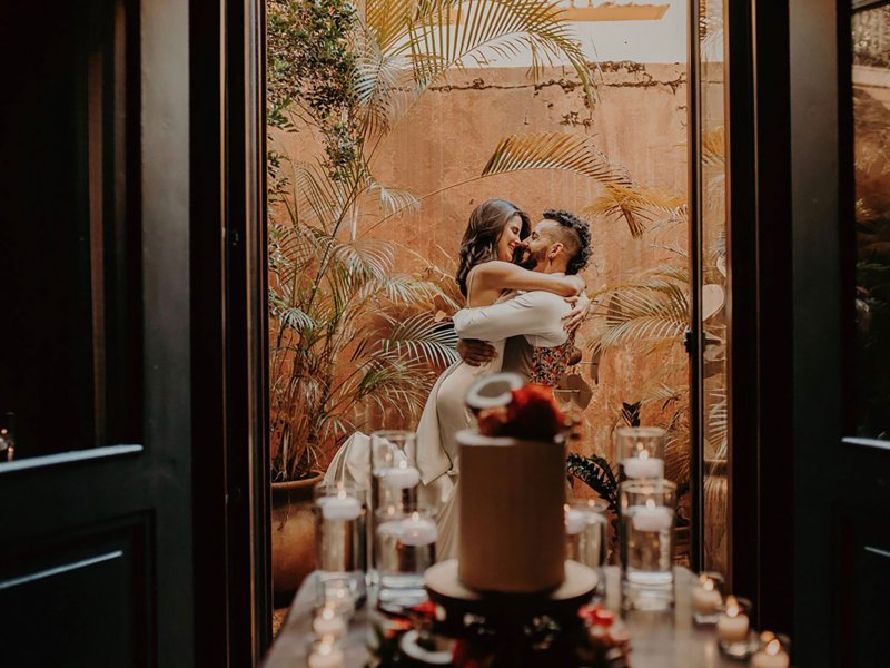 Una pareja se abraza en un balcón con un pastel de bodas en primer plano en El Convento en San Juan, Puerto Rico.