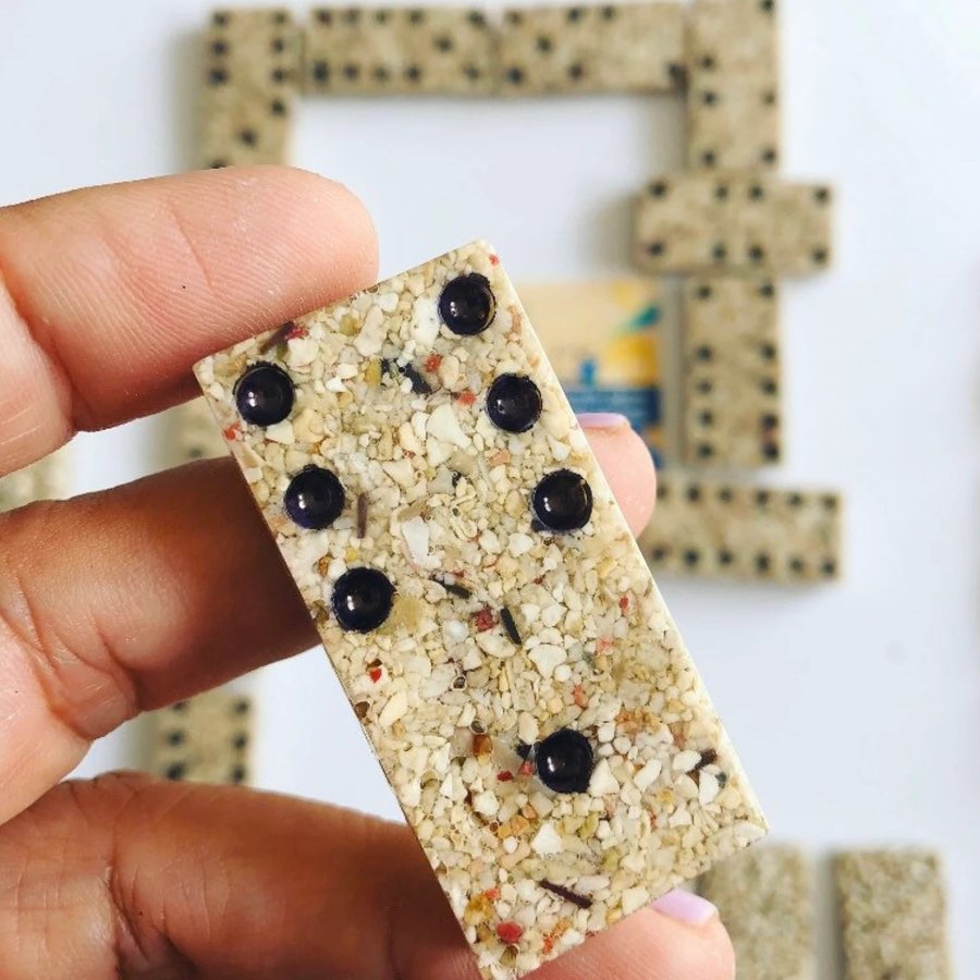 Close up of a hand holding a Puerto Rican sand domino, with additional game pieces seen in the background.