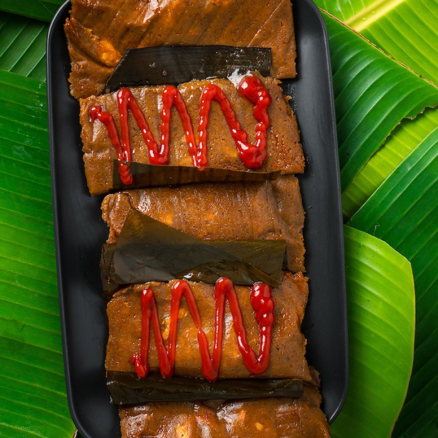 Plate of pasteles with and without ketchup on top of banana leaves.