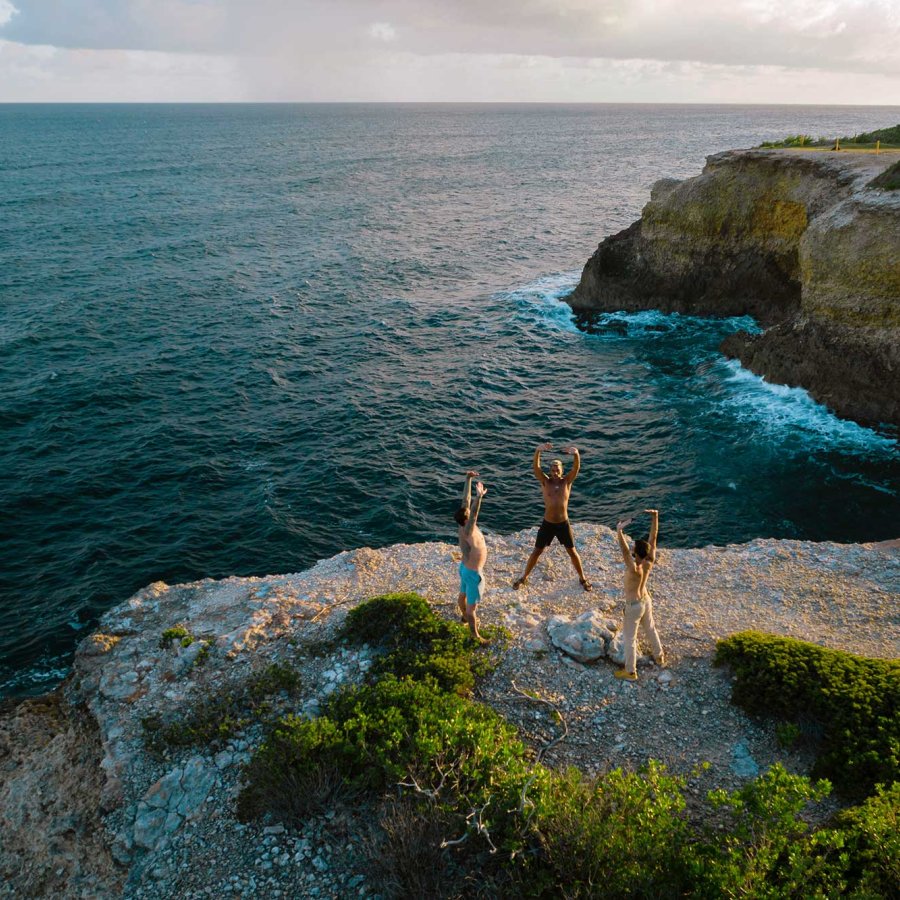 Three people practice yoga on an oceanside cliff during a retreat at Finca Victoria. Vieques, Puerto Rico.