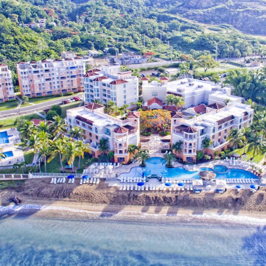Vista aérea de un gran complejo frente al mar con colinas verdes detrás. Rincón Beach Resort, Añasco, Puerto Rico.